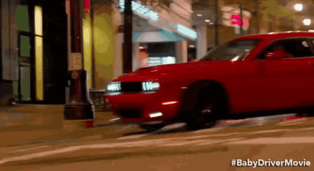 a red car is driving down a city street at night