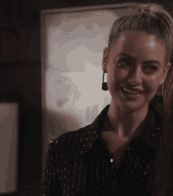 a woman wearing a black shirt and earrings smiles in front of a painting
