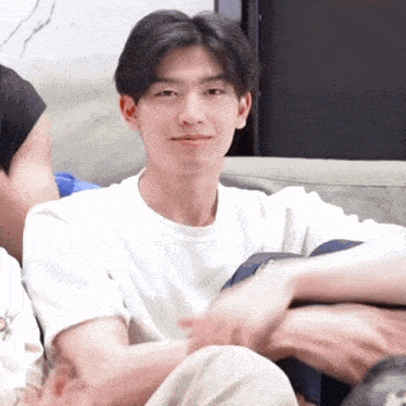a young man in a white shirt is sitting on a couch with his legs crossed .