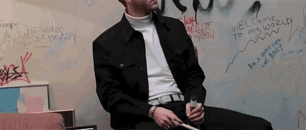 a man sitting in front of a wall with graffiti on it that says welcome to my world