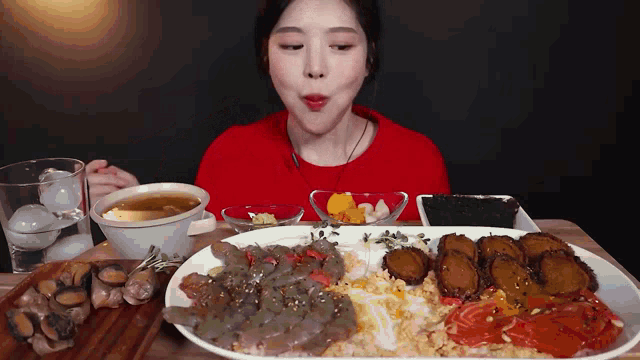 a woman in a red shirt is eating a plate of food on a table