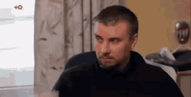 a man with a beard is sitting in a chair in a living room and making a funny face .