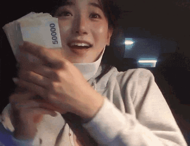 a woman wearing a face mask is holding a stack of money that says 50000 on it