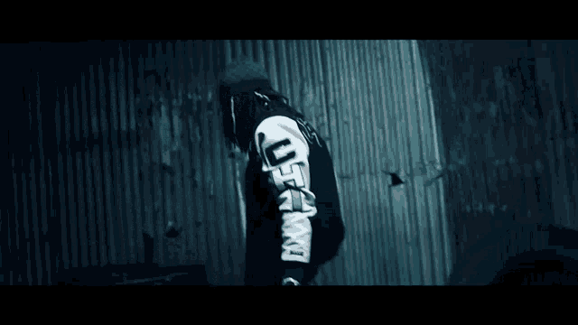 a man with dreadlocks is standing in front of a metal wall wearing a black and white jacket .