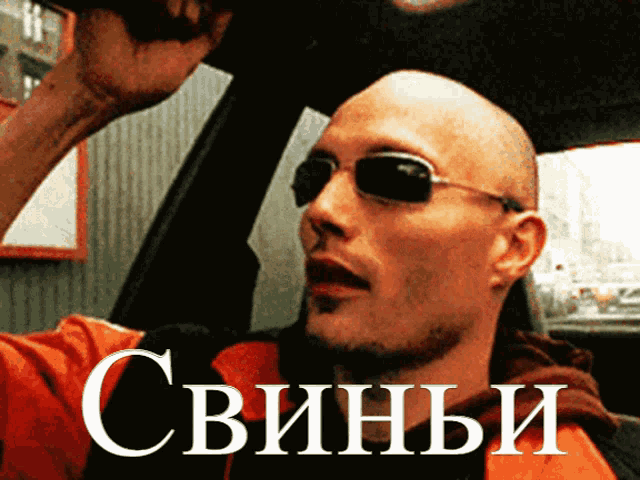 a man wearing sunglasses is sitting in a car with the word свиньи written on the bottom