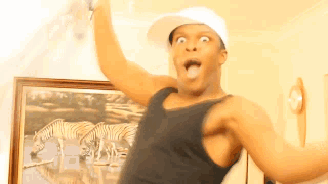 a man wearing a white hat and a black tank top is standing in front of a picture of zebras