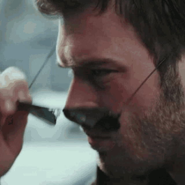 a man with a beard is wearing glasses and holding a pen to his nose .