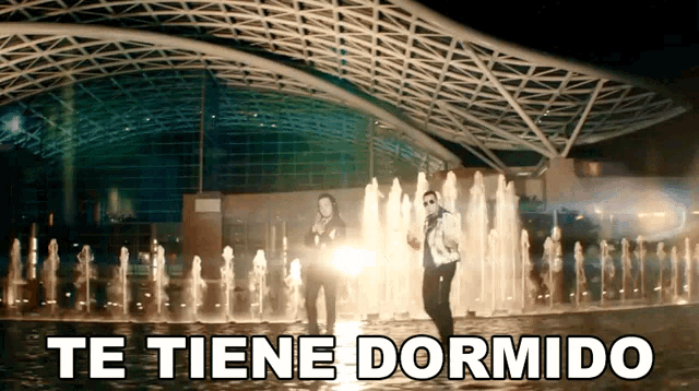 two men are dancing in front of a fountain and the caption te tiene dormido