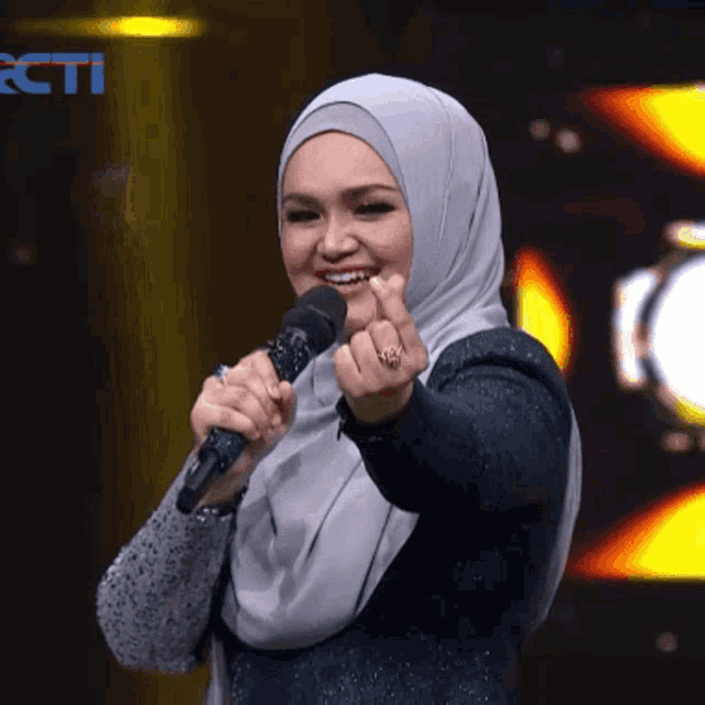 a woman wearing a hijab is holding a microphone in front of a rcti logo