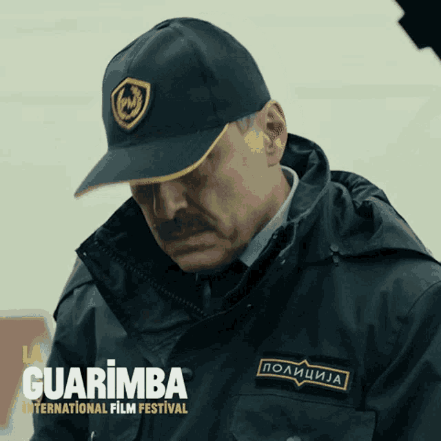 a man with a mustache wearing a hat and a jacket with guarimba international film festival on the bottom