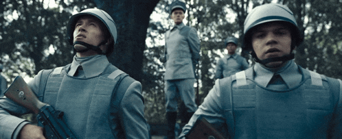 a group of soldiers are standing in a line and one of them has a gun with the letter c on it