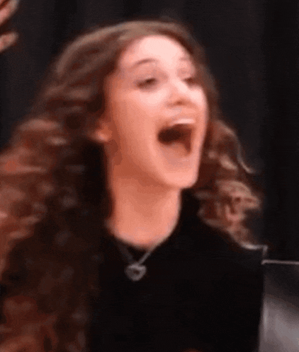 a woman with long curly hair is laughing with her mouth wide open .