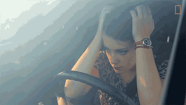 a woman with a watch on her wrist is sitting in the driver 's seat of a car