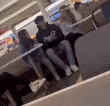 a group of people are sitting at tables in a restaurant . one of the people is wearing a coca cola sweatshirt .