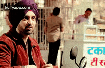 a man in a turban is sitting on a motorcycle and talking to someone .