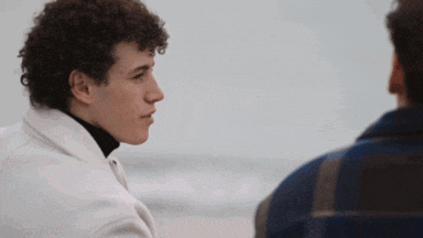 a man with curly hair is talking to another man in a plaid jacket