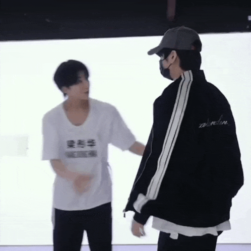 two men are standing next to each other in front of a white wall .