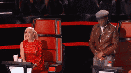 a woman in a red dress is sitting in a red chair with her hands up .