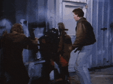 a man in a brown jacket is standing next to a man in a black helmet