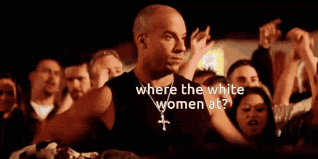 a man with a cross necklace stands in front of a crowd asking where the white women are