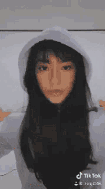 a woman with long black hair is wearing a white hoodie and looking at the camera .