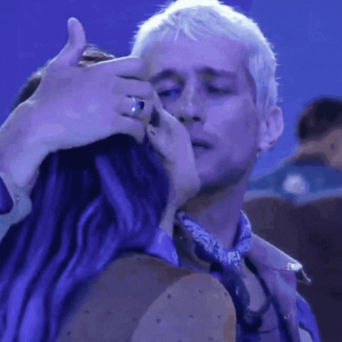 a man and a woman with purple hair are hugging each other in front of a blue background .