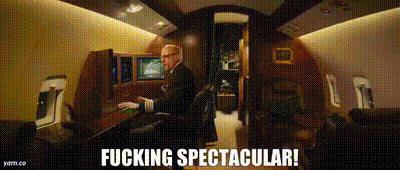 a man in a suit is standing in a room with the words fucking spectacular written below him .