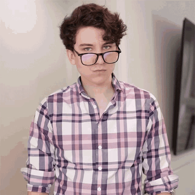 a young man wearing glasses and a plaid shirt is looking at the camera