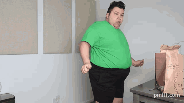 a man in a green shirt is standing next to a bag that says chipotle on it