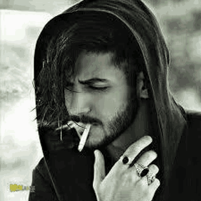 a man with a beard is smoking a cigarette and wearing a hoodie .