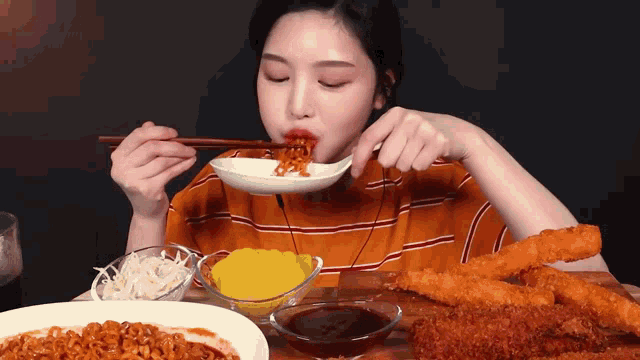 a woman is eating noodles with chopsticks at a table full of food