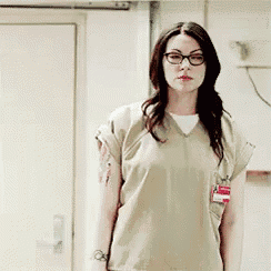 a woman wearing glasses and a scrub top is standing in a room .