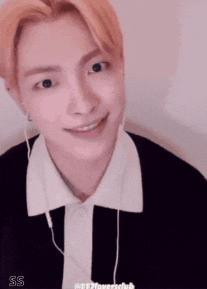 a young man with blonde hair is smiling with his eyes closed and wearing earphones .