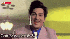 a man in a suit and tie is smiling in front of a sign that says ' telugu movies '