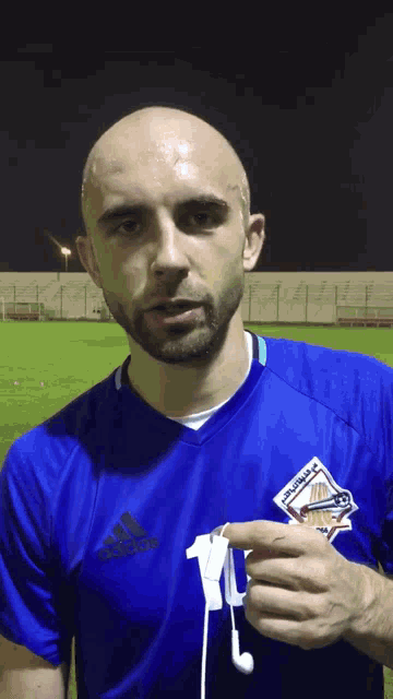 a man wearing a blue adidas shirt is holding a pair of earbuds