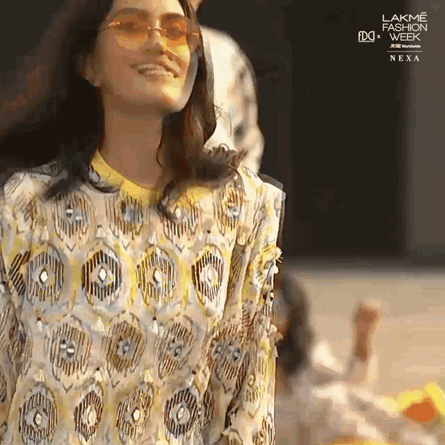 a woman wearing sunglasses and a patterned shirt is smiling at the camera