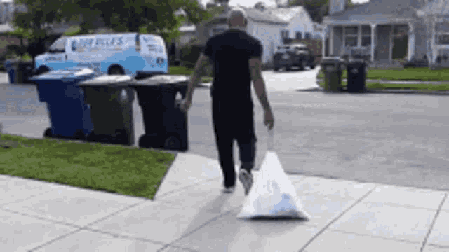 a man is walking down a sidewalk carrying a large bag of trash
