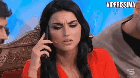 a woman in a red shirt is talking on a cell phone while sitting on a couch .