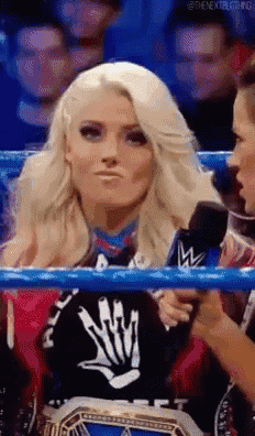 a woman is sitting in a wrestling ring holding a microphone and making a face .