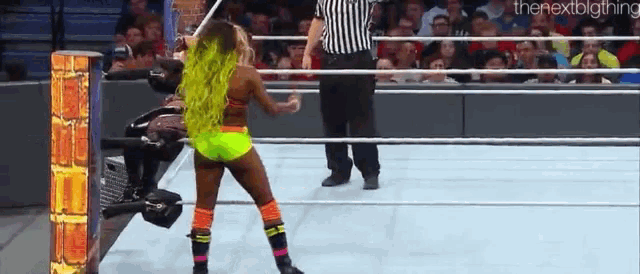 a woman with green hair is standing in the middle of a wrestling ring .