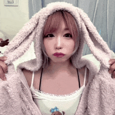 a woman wearing bunny ears and a white tank top looks at the camera