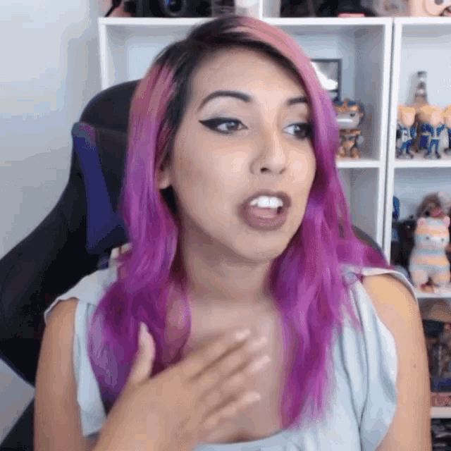 a woman with purple hair is sitting in front of a shelf with toys on it .