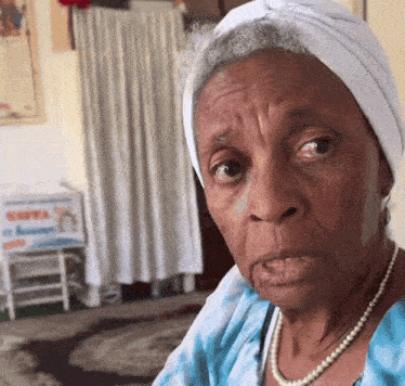 a woman wearing a turban and a pearl necklace looks at the camera