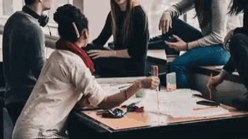 a group of young people are sitting around a table talking .