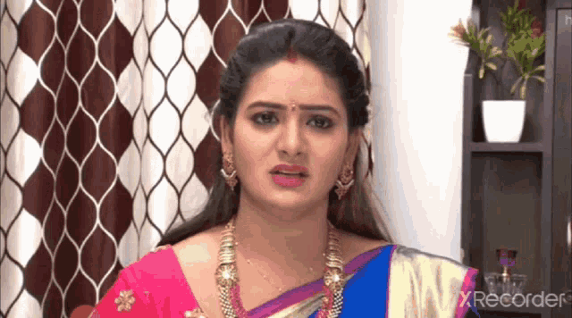 a woman in a pink and blue saree is making a funny face in front of a screen that says xrecorder