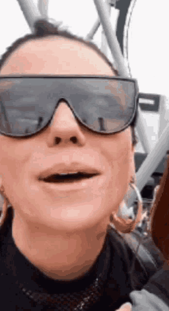 a woman wearing sunglasses and hoop earrings is making a funny face .