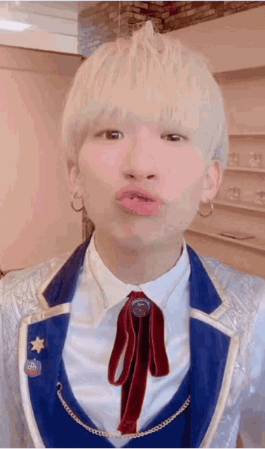 a young man with blonde hair is wearing a suit and tie and making a funny face .