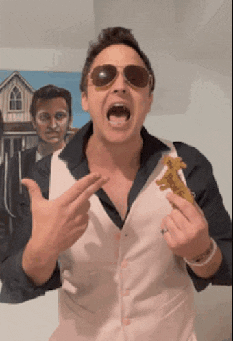 a man wearing sunglasses and a vest holds a piece of food