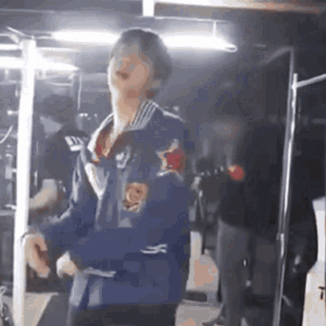 a man in a blue jacket is dancing in a dark room in front of a camera .