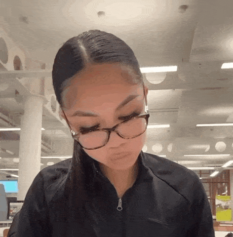 a woman wearing glasses and a black jacket is looking down at something .